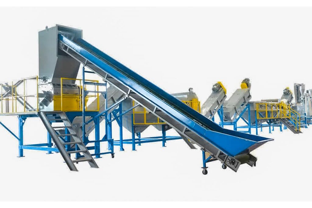 this appears to be a plastic recycling line or system used for sorting, processing and recycling various types of plastic waste materials. The main components visible are: 1) A large inclined conveyor belt or ramp, likely for feeding in mixed plastic waste streams. 2) Several sorting stations or units with rotating cylindrical screens or trommels, which can separate materials by size. 3) Additional conveyor belts and chutes to transport and direct different sorted plastic fractions. 4) An enclosed housing or control room section at the head of the system. This type of integrated recycling line allows mixed plastic waste to be efficiently sorted by methods like screening, air separation, and potentially automated optical sorting. Different sorted plastic types like bottles, films, rigid plastics etc. can then be further processed separately through shredding, washing, and pelletizing operations to produce recycled plastic resin/pellets as the final output product. Such industrial-scale sorting and recycling systems are critical for effectively recovering and recycling large volumes of post-consumer and post-industrial plastic scrap/waste in an automated, controlled fashion.