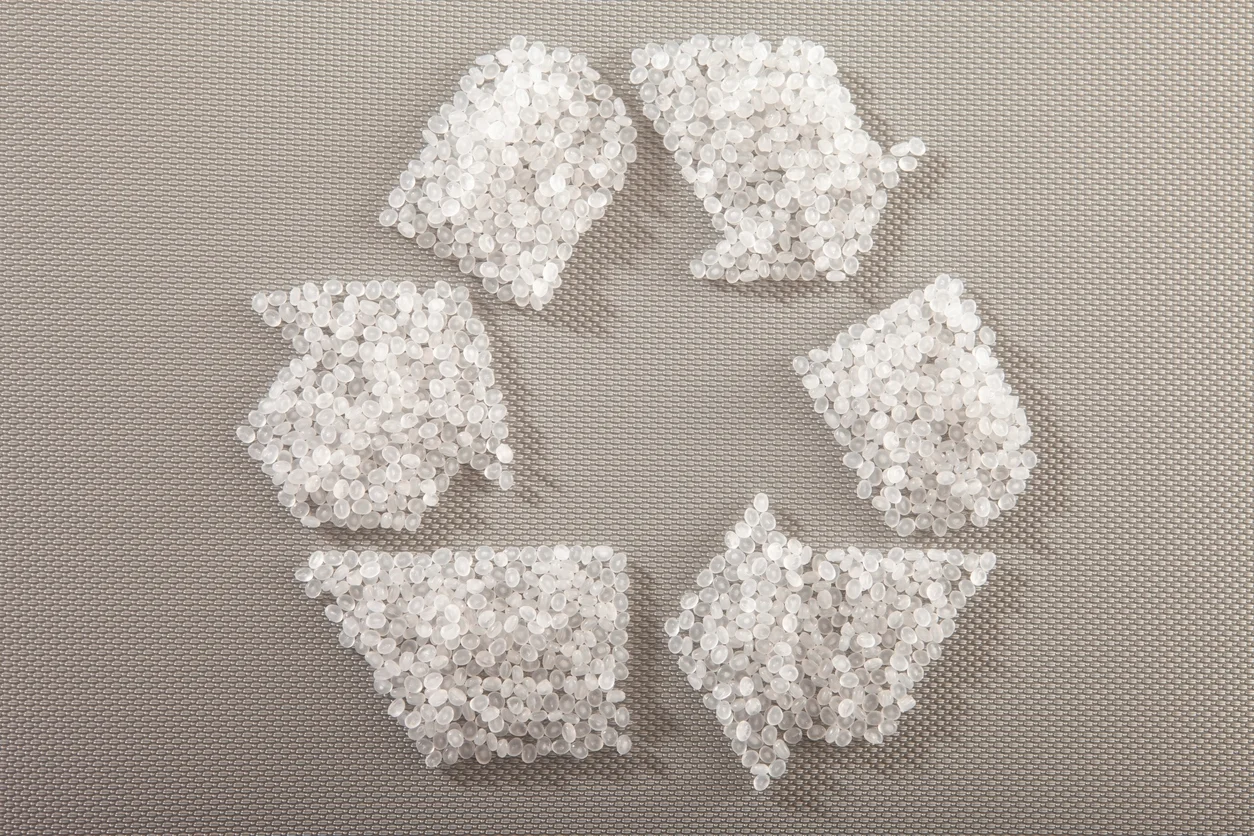 Das Bild zeigt kleine, durchsichtige Kunststoffpellets, die in der Form des universellen Recyclingsymbols angeordnet sind.